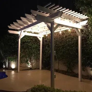 A white pergola is lit up at night in a backyard.