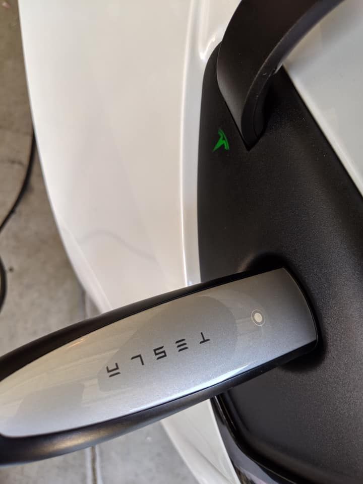A tesla charger is plugged into a white car
