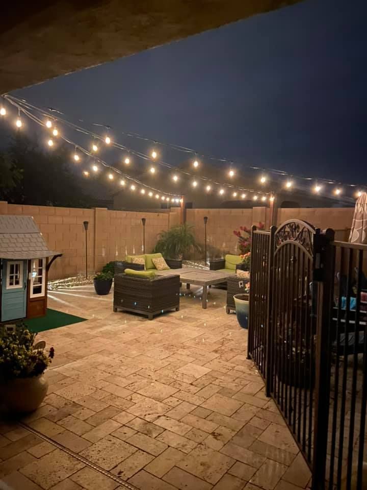 A patio with a lot of furniture and lights hanging from the ceiling at night.