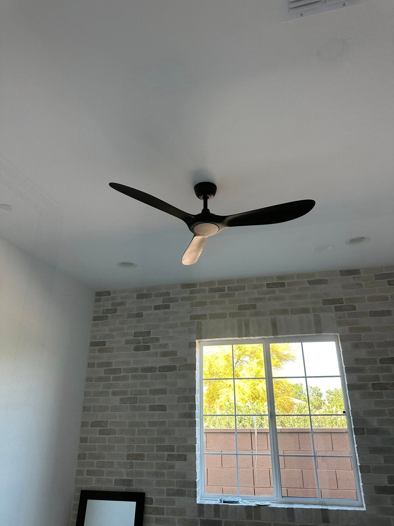 A ceiling fan is hanging from the ceiling in a room with a brick wall.