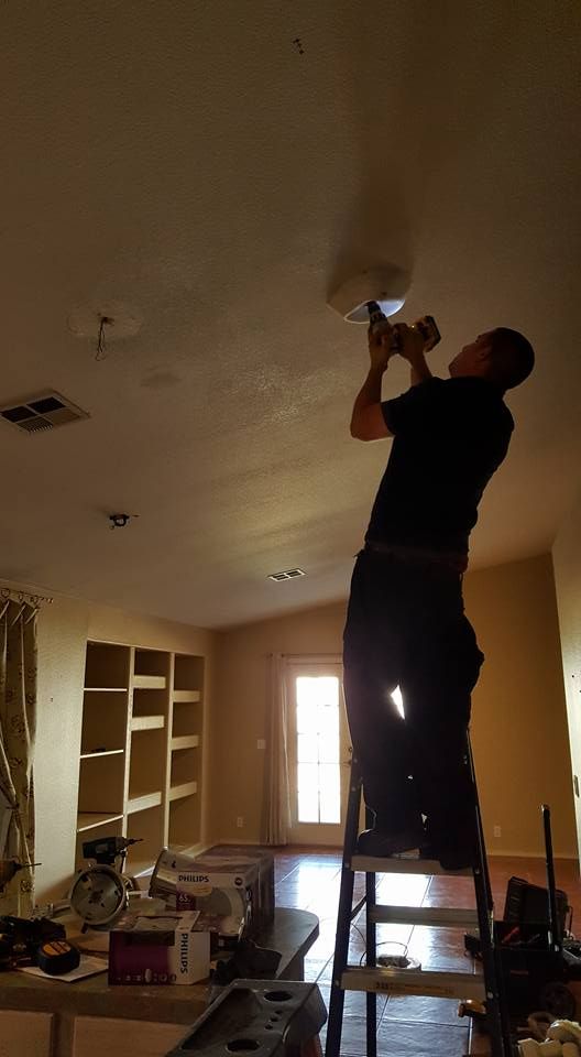 A man is standing on a ladder fixing a light fixture in a living room.