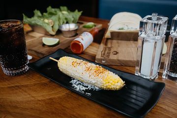 A corn on the cob on a stick on a black plate on a table.