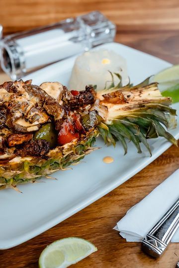 A white plate topped with a pineapple filled with meat and vegetables.