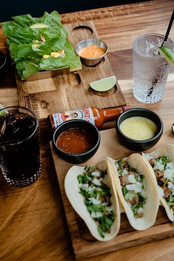 A wooden cutting board topped with tacos and sauces on a table.
