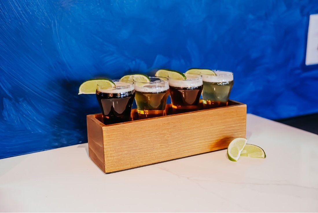 A wooden tray filled with shot glasses and lime wedges.