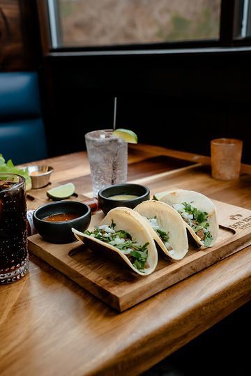 A wooden cutting board topped with tacos and a drink on a table.