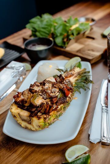A pineapple filled with meat and vegetables is on a white plate on a wooden table.