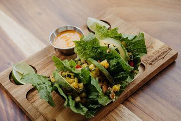 A wooden cutting board topped with lettuce, avocado, and sauce.
