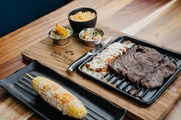 A wooden table topped with plates of food including corn on the cob and steak.