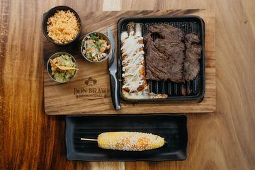 A wooden table topped with plates of food and a corn on the cob.
