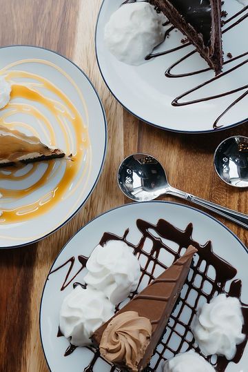 Two plates of desserts with whipped cream and chocolate sauce on a wooden table.