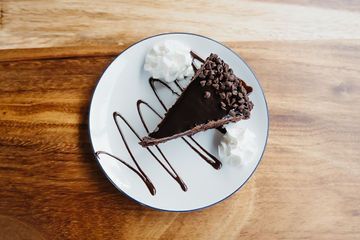 A slice of chocolate pie with whipped cream on a white plate on a wooden table.