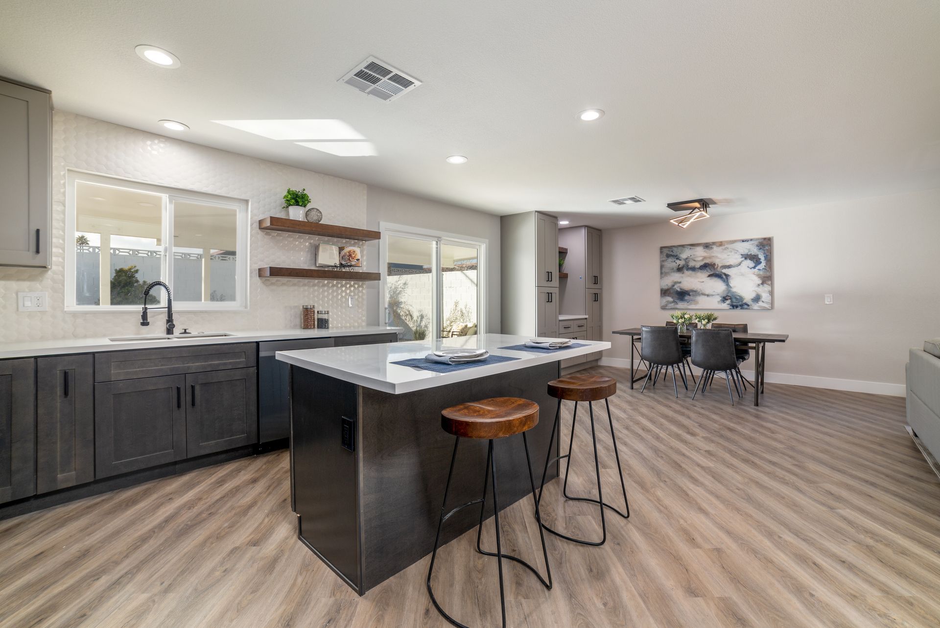 Modern kitchen with gray cabinets, island with stools, and dining area with artwork.