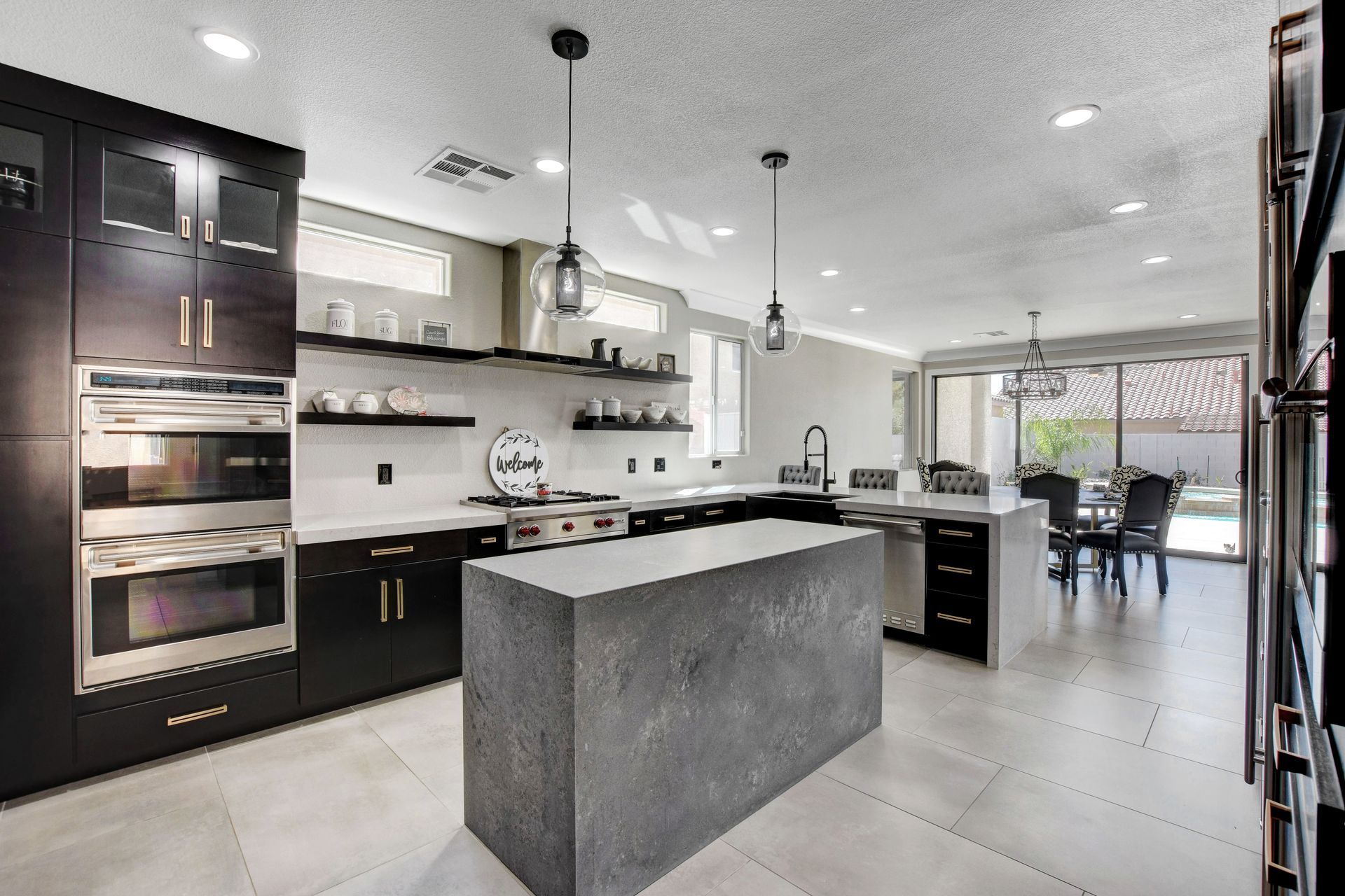 Modern kitchen with dark cabinets, concrete island, and stainless steel appliances.