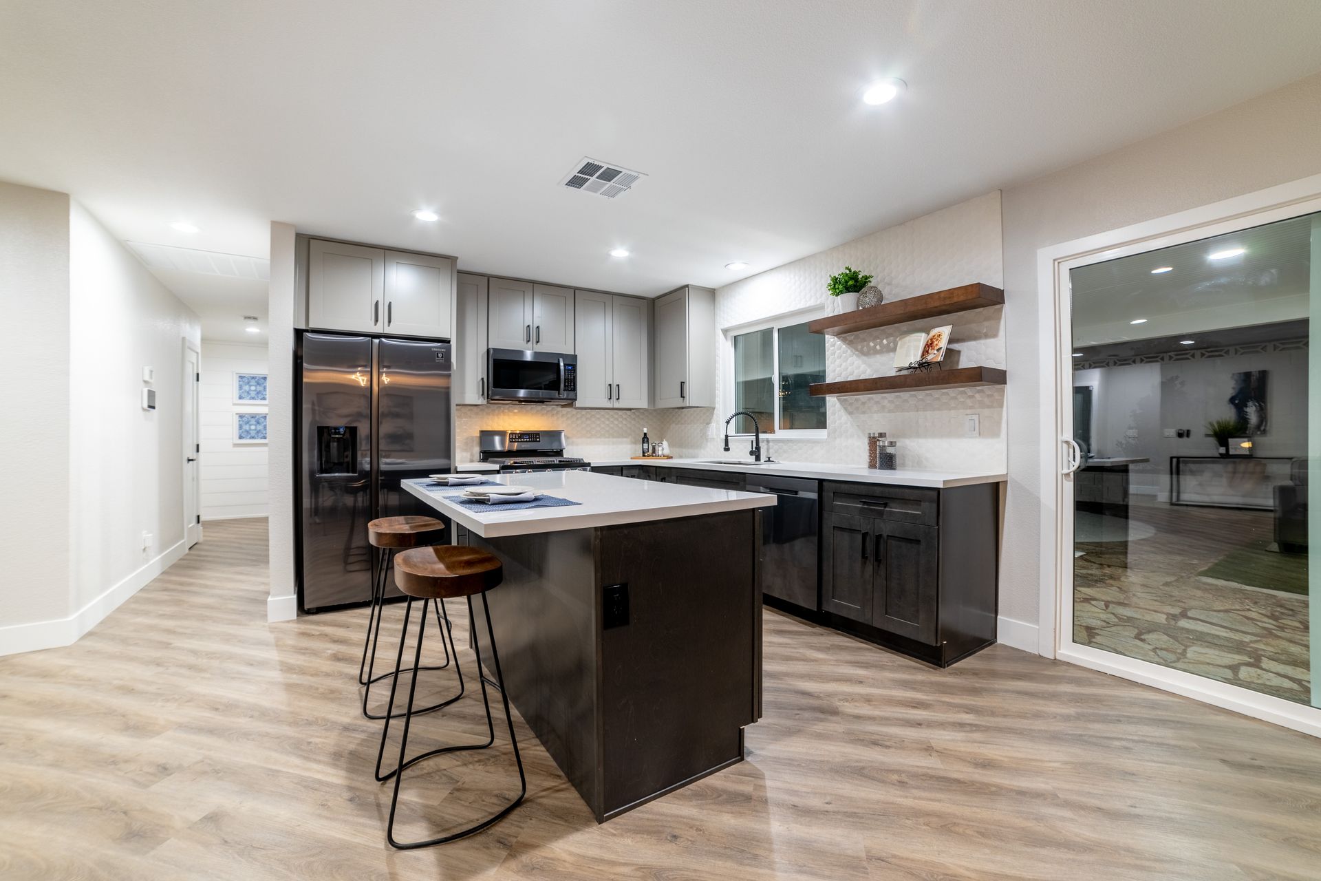 Modern kitchen with gray cabinets, island with stools, and black appliances.