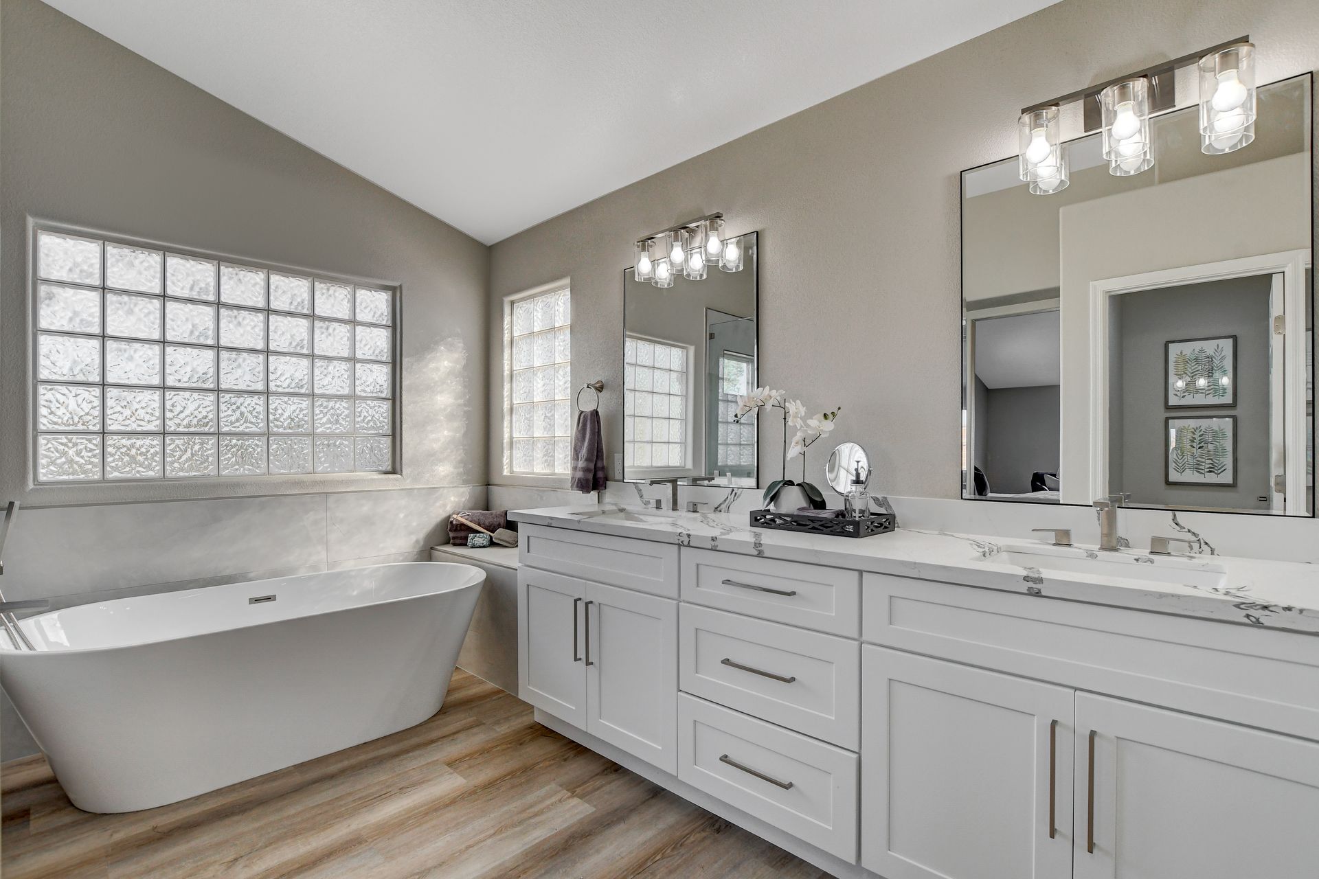 Modern bathroom with a white bathtub, vanity, and glass block window.