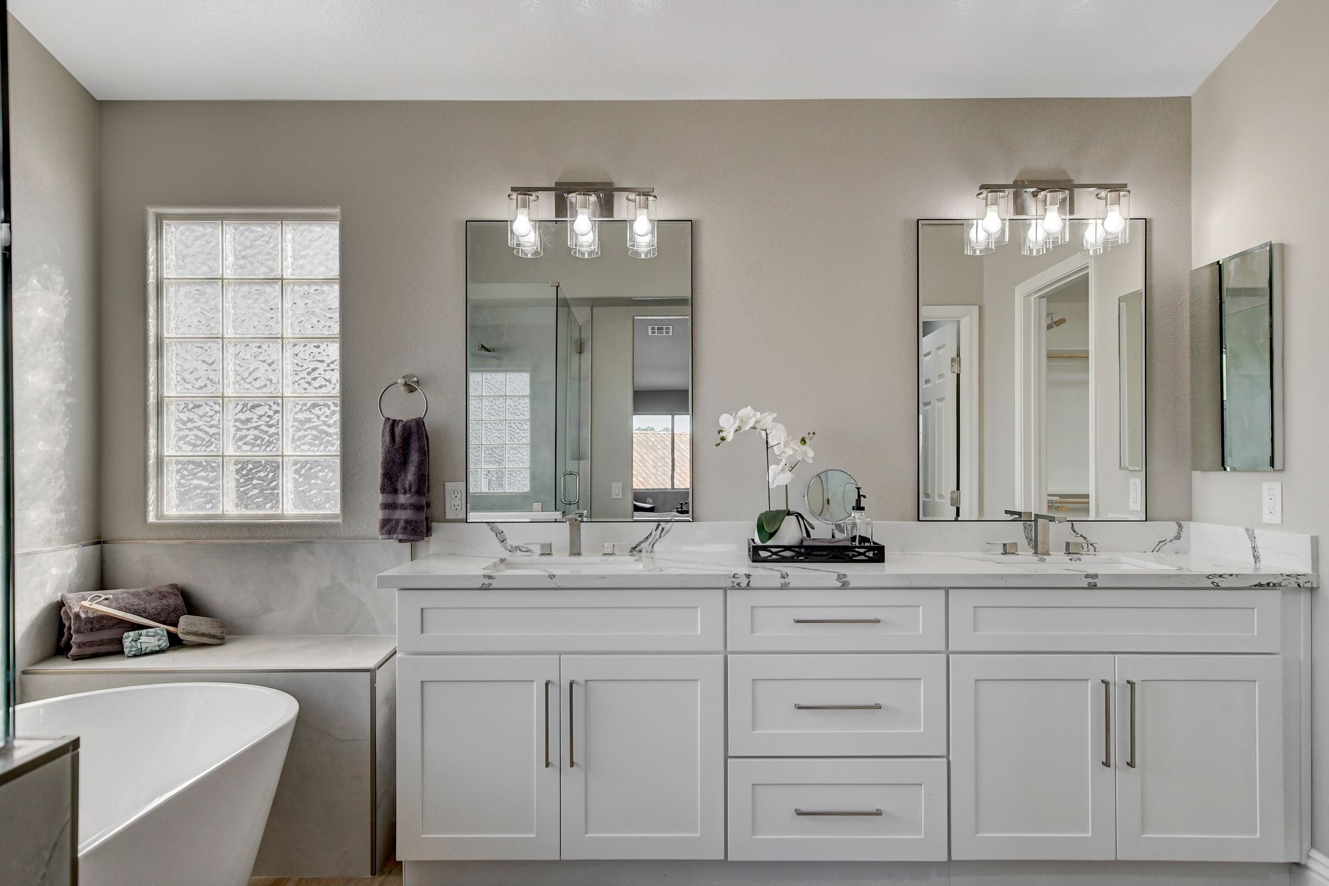 Modern white bathroom with double vanity, bathtub, and large mirrors.
