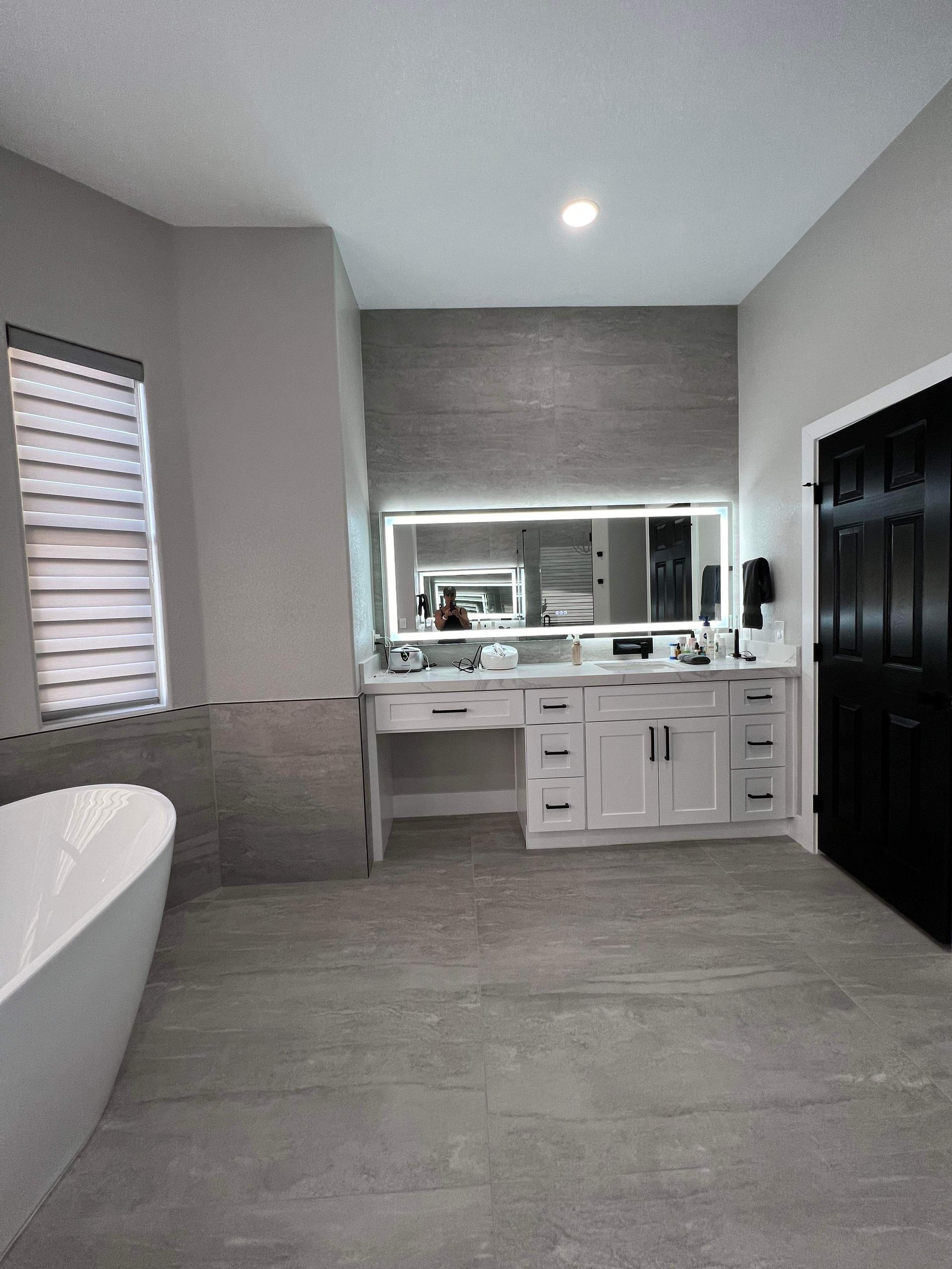Modern bathroom with freestanding tub, white vanity, gray tile, and black door.