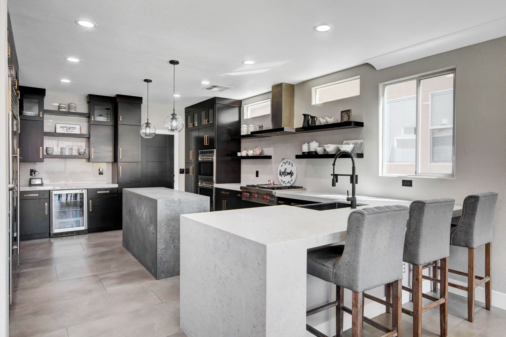 Modern kitchen with dark cabinetry, gray islands, and light countertops. Bar stools face island.