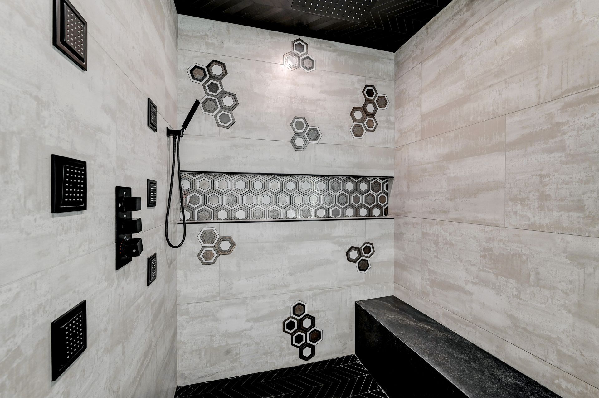 Modern shower with light gray tile, black fixtures, and decorative honeycomb accents. Bench seating.