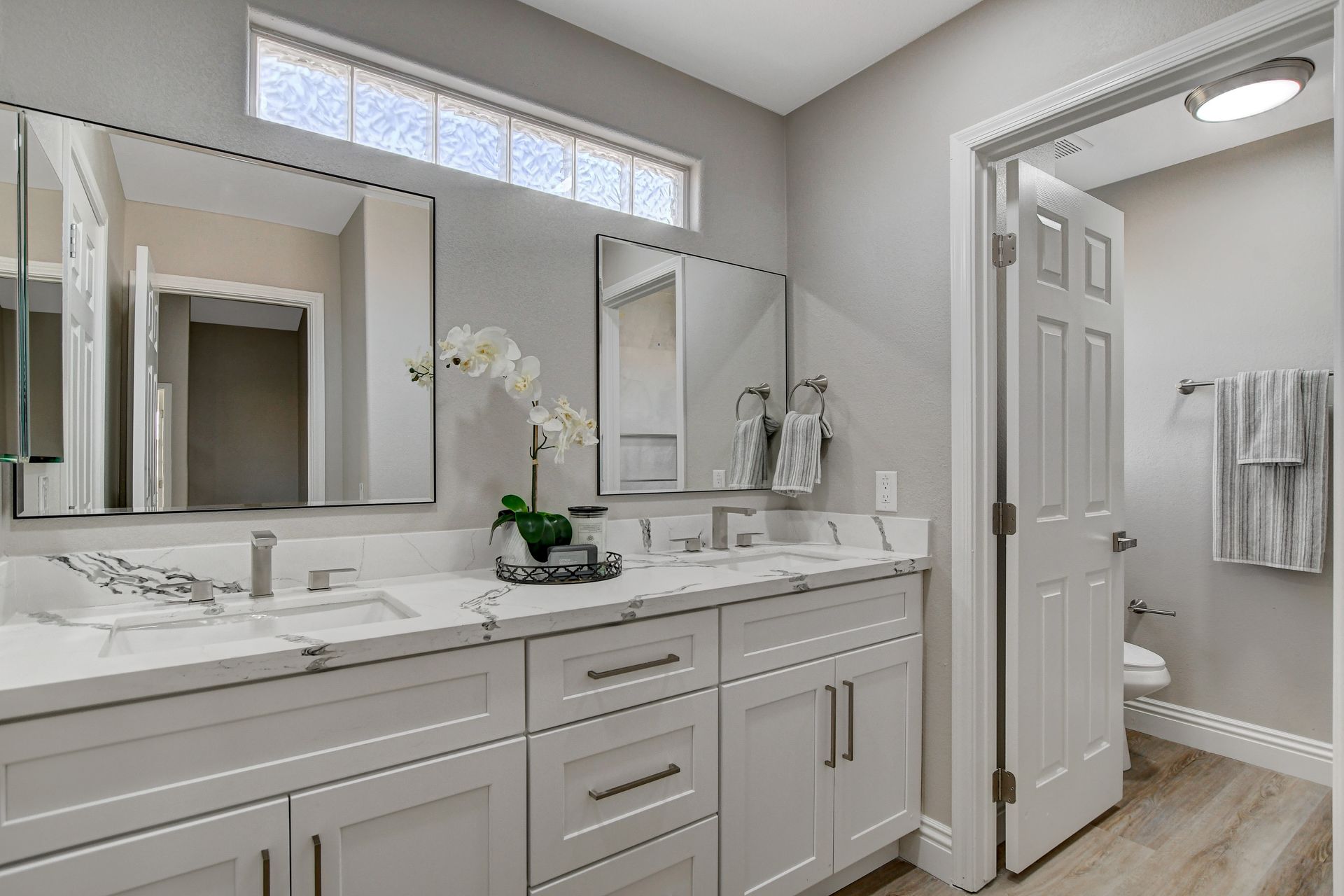 Bathroom with white double vanity, large mirrors, and open door to the right.