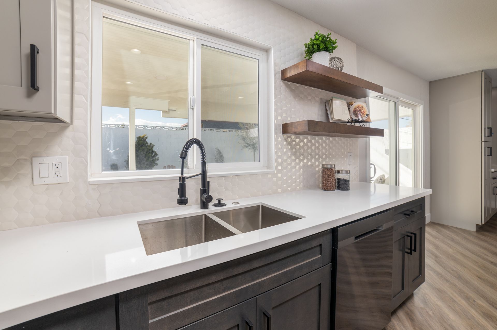 Kitchen with white countertops, dark cabinets, a stainless steel sink, and wooden shelves.