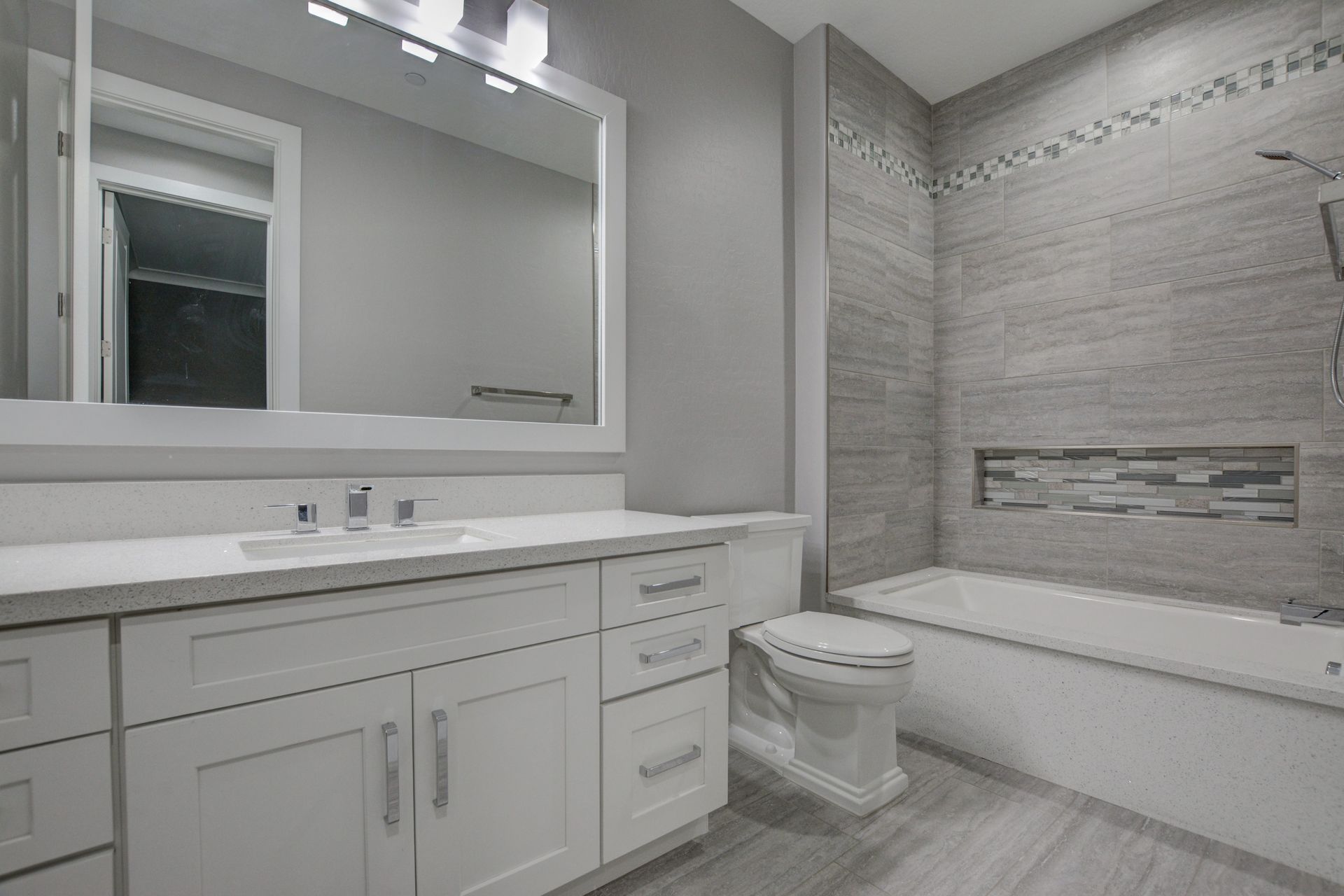 White bathroom with a vanity, toilet, and bathtub with gray tiled walls.