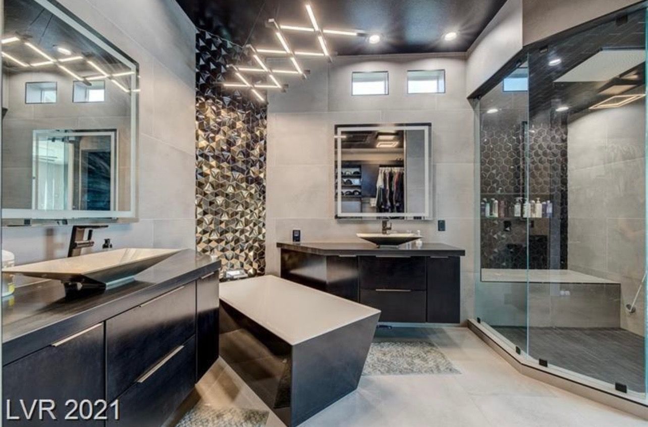 Modern bathroom with black cabinetry, geometric wall, shower, and angled bathtub.