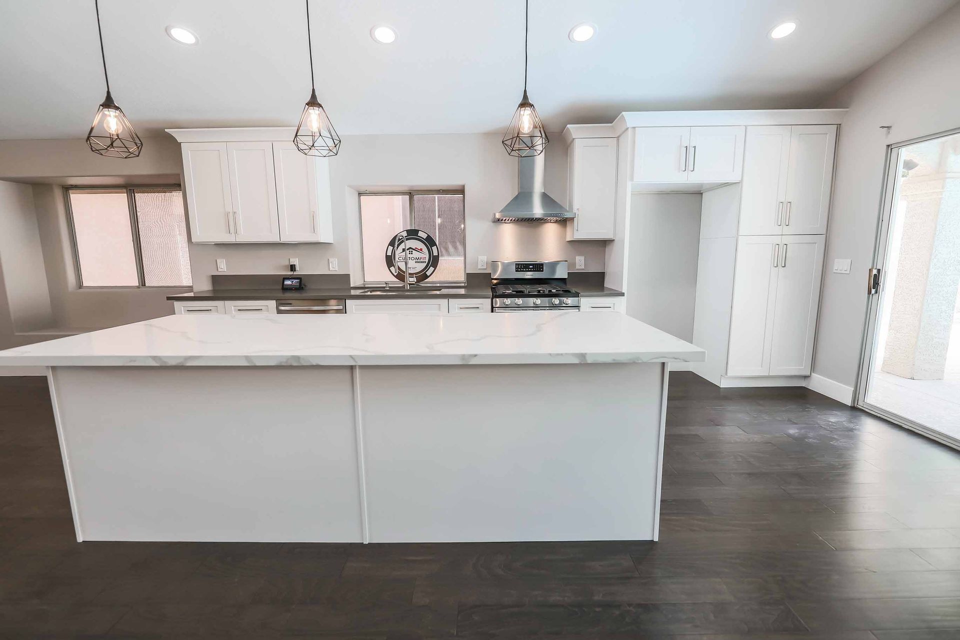 Modern kitchen with white cabinets, island, stainless steel appliances, and dark wood floors.