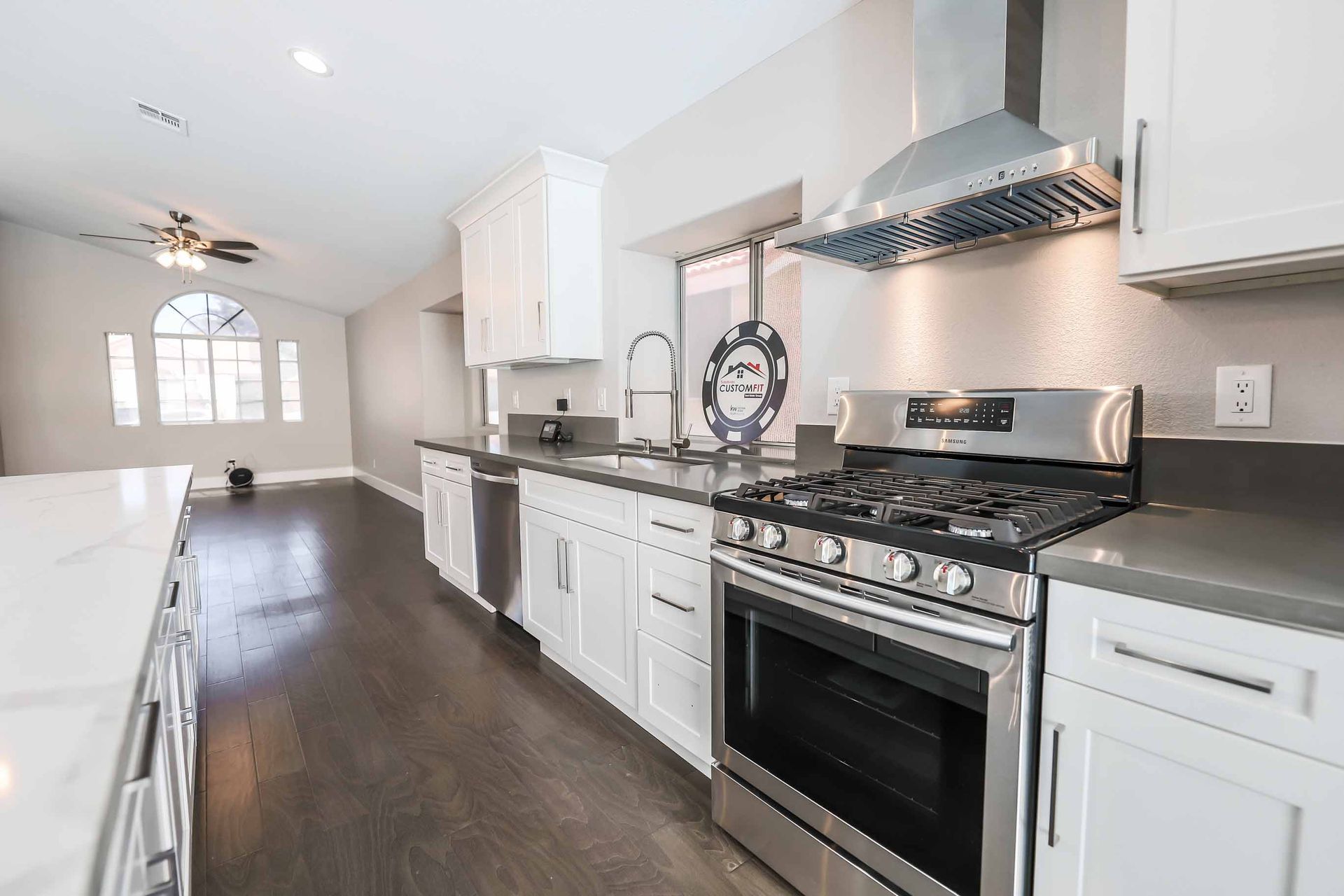Modern white kitchen with stainless steel appliances, dark wood floors, and gray countertops.