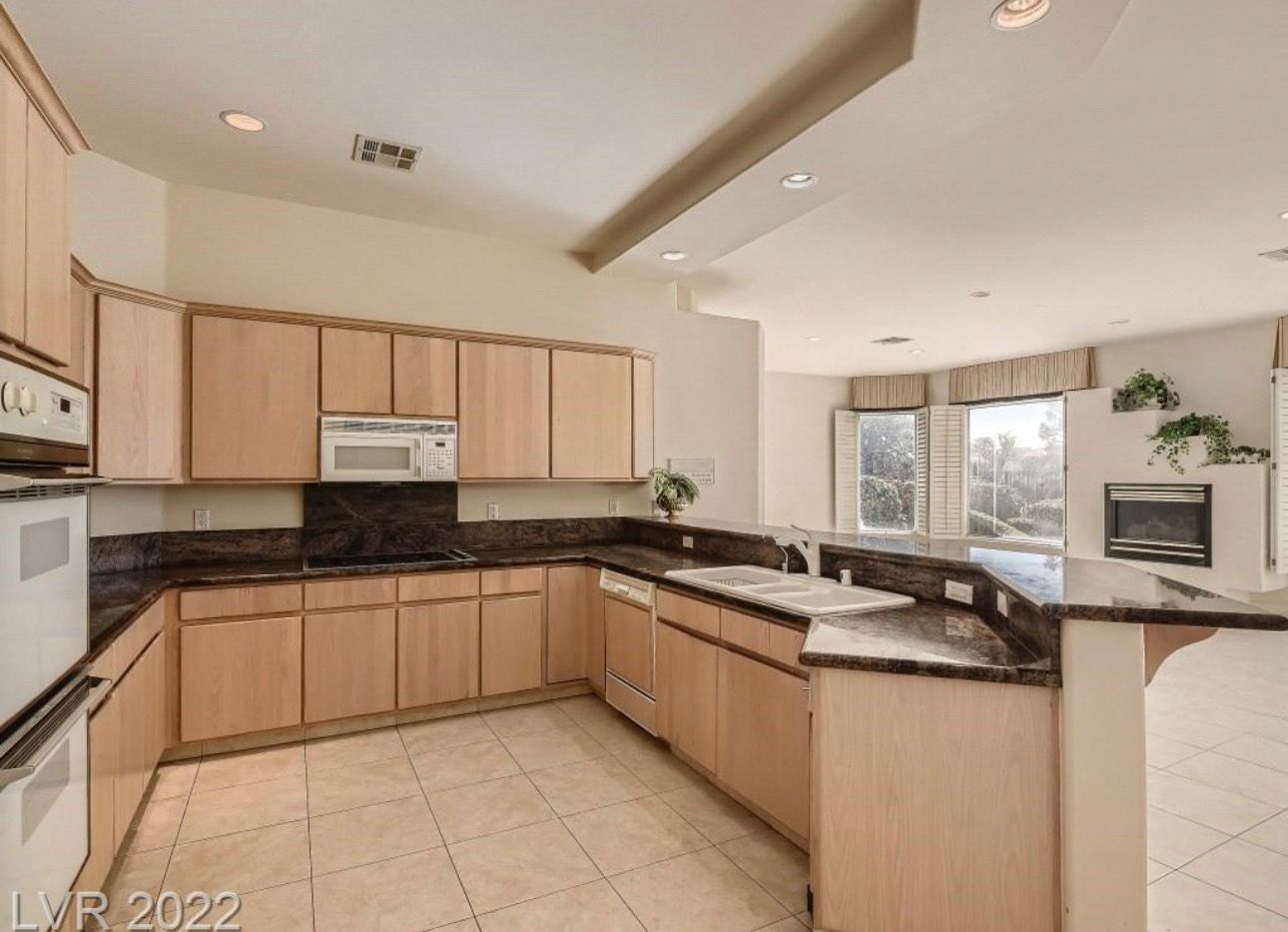 Kitchen with light wood cabinets, dark countertops, and tile floor. Includes oven, microwave, and sink.