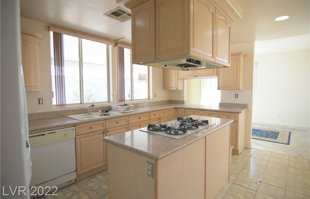 Kitchen with light cabinets, an island with a stovetop, and a window over the sink.