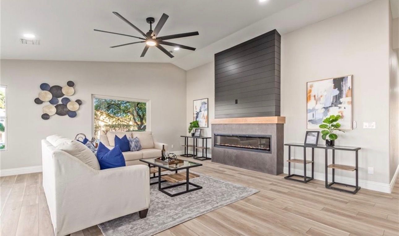 Living room with white sofas, fireplace, artwork, and ceiling fan.