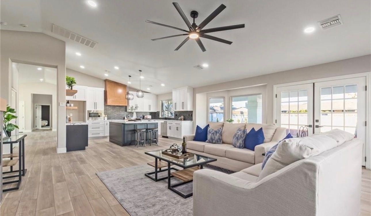 Open-concept living space with kitchen and living room. Neutral colors, wood floors, and a large ceiling fan.