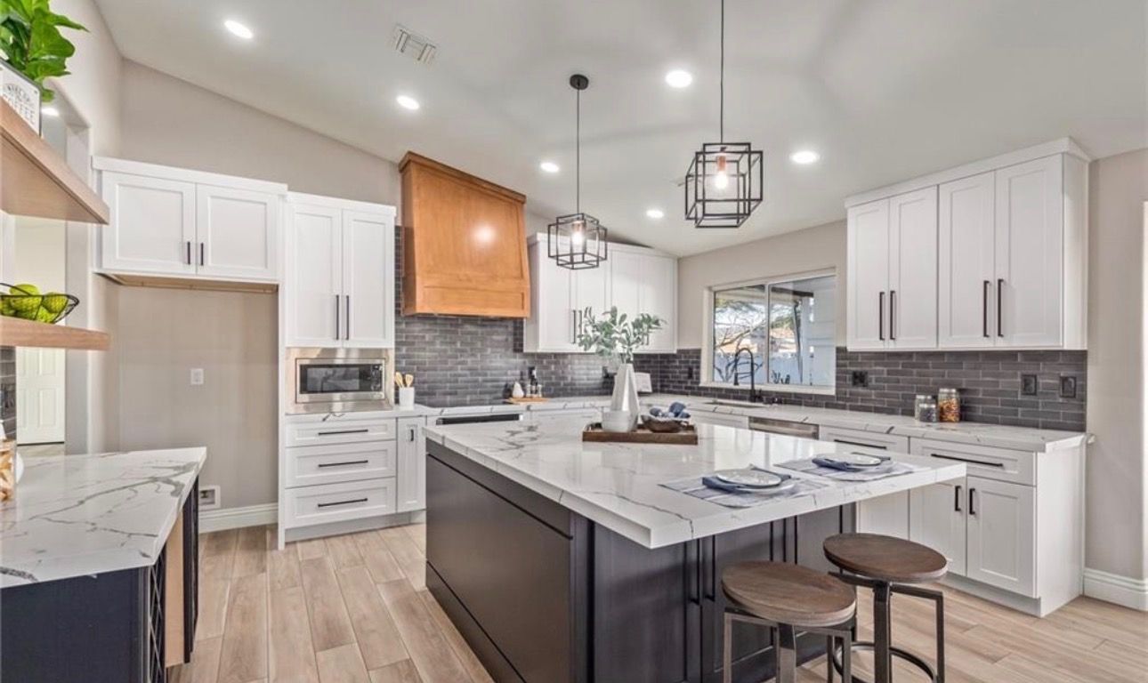 Modern kitchen with white cabinets, dark island, granite countertops, and wood accents.
