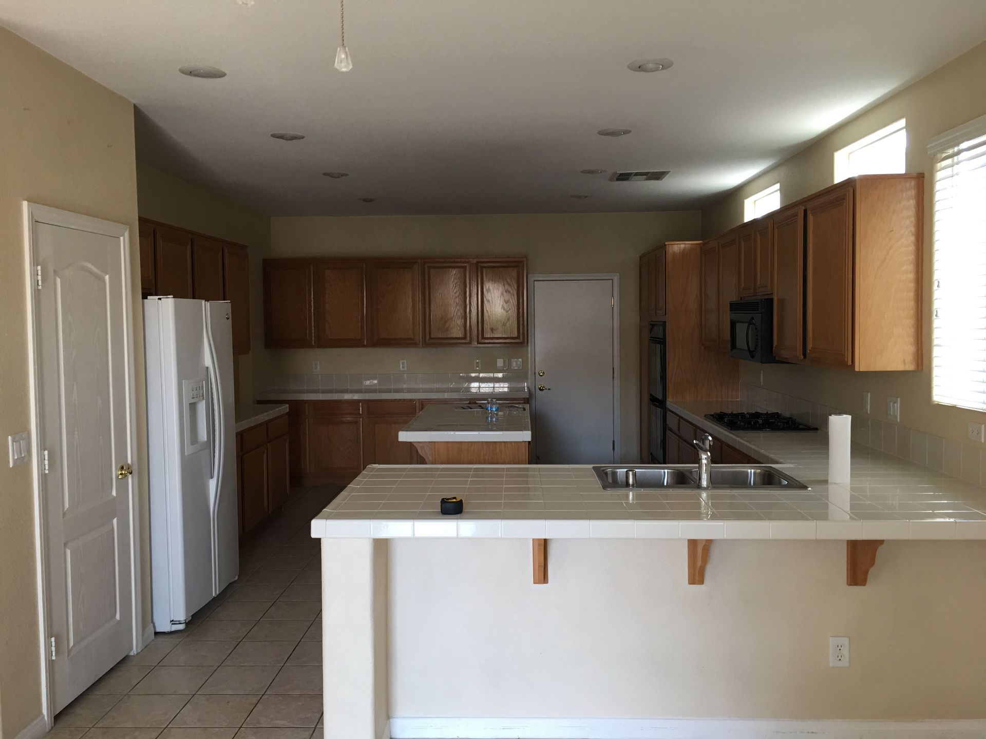 Kitchen with wood cabinets, light countertops, and tile floor. White refrigerator and island.
