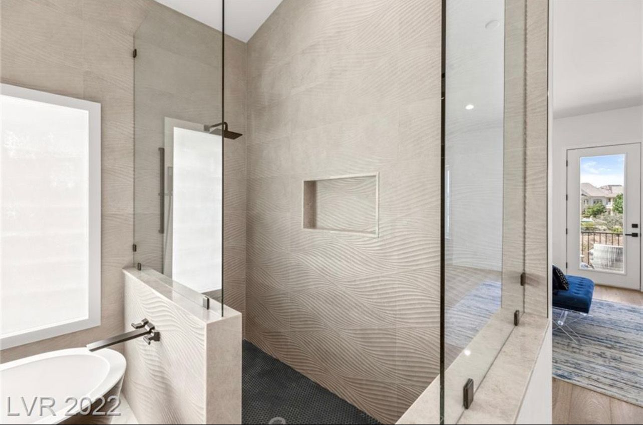Modern bathroom with textured gray tile shower, glass enclosure, and a partial wall separating it from a white bathtub.