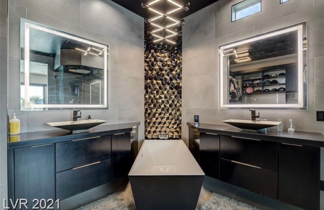 Modern bathroom with two sinks, black cabinets, and a decorative gold-toned accent wall.