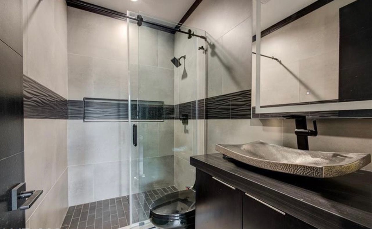Modern bathroom with walk-in shower, dark wood vanity, stone vessel sink, and gray tile walls.