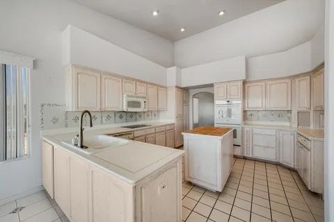 Cream-colored kitchen with white countertops, island, cabinets, and tile flooring. A built-in oven and microwave are visible.