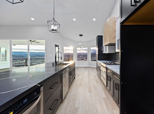 Modern kitchen with dark cabinetry, large island, and city view through windows.
