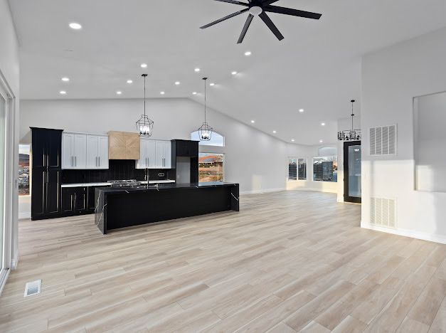 Open-concept kitchen with black island, light wood floor, white walls and ceiling, recessed lighting, and black cabinets.