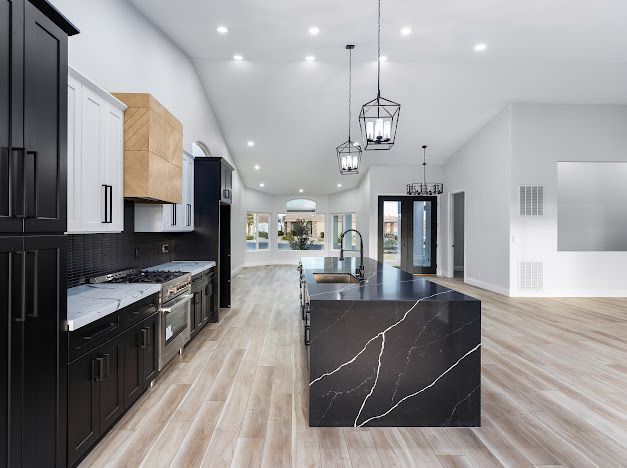 Modern kitchen with black island, cabinets, light wood floor, and high ceiling.
