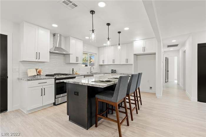 Modern kitchen with white cabinets, dark gray island, and light wood flooring.