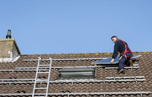 Worker on a tiled roof using a ladder beside a skylight on a sunny day