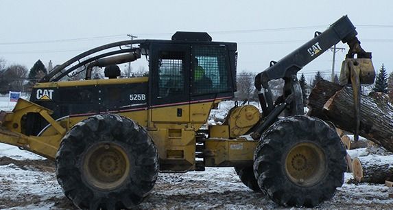 A cat tractor is carrying logs in the snow