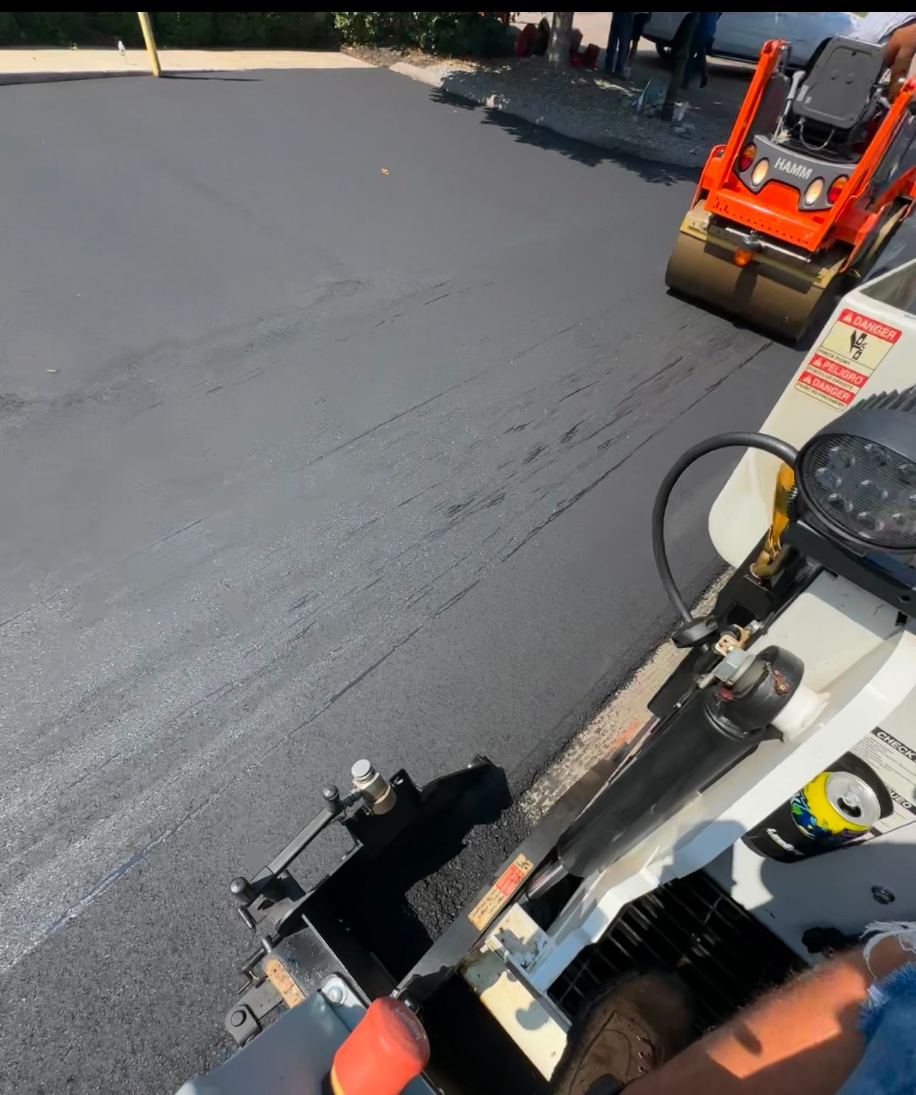 A person is driving a machine on a road that says ' asphalt ' on it