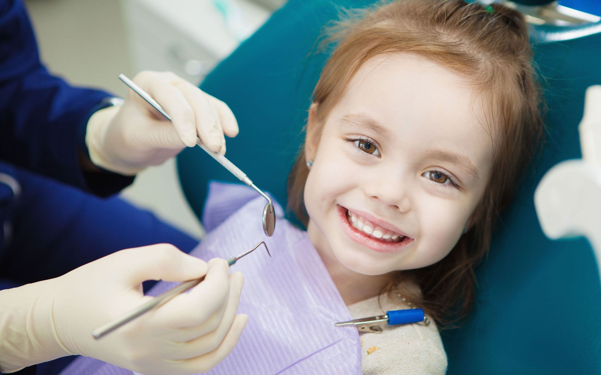 a little girl is sitting in a dental chair while a dentist examines her teeth