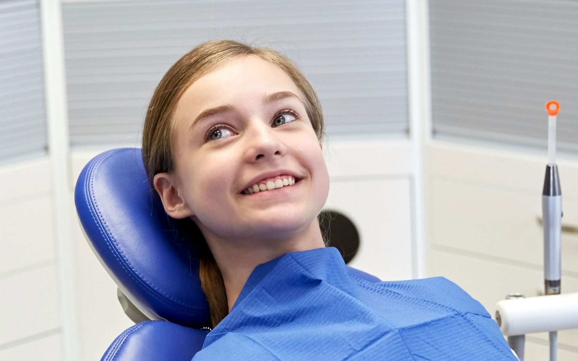 a young girl is sitting in a dental chair and smiling