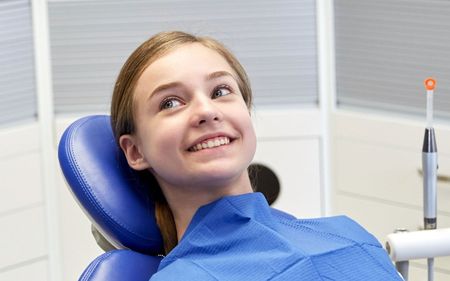 a young girl is sitting in a dental chair and smiling